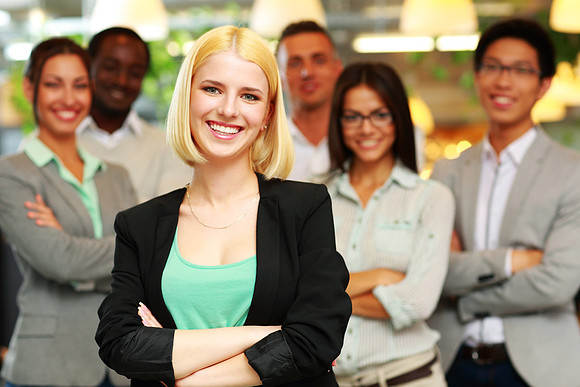 Cheerful businesswoman with arms folded standing in front her colleagues